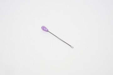 ear pick made of stainless steel with a purple plastic handle from the side angle on a white background