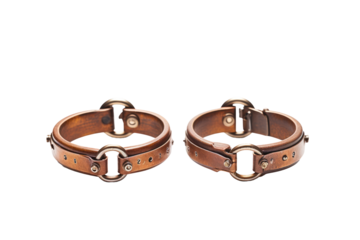 A pair of brown leather cuffs with sturdy metal buckles are displayed against a plain background. The cuffs feature intricate stitching and high quality craftsmanship.