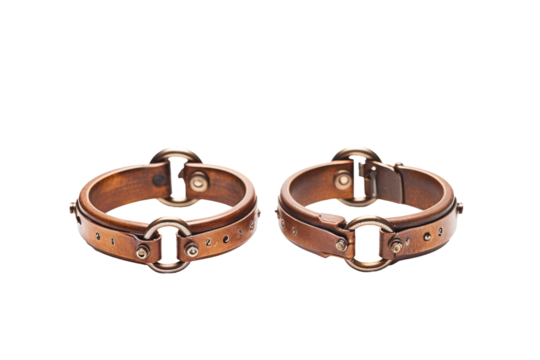 A pair of brown leather cuffs with sturdy metal buckles are displayed against a plain background. The cuffs feature intricate stitching and high quality craftsmanship.