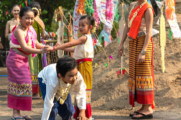 Boy and girls in traditional Thai clothing playing together at sand castle during Song kran...