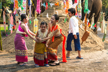 Fototapeta na wymiar Thai boy and girls in traditional Thai dresses playing near sand castle decorating with colorful flags during Song Kran festival in chiangmai, Thailand 