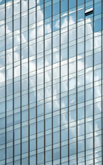 windows of modern office building exterior reflects cloudy sky.