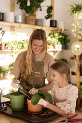 Vertical medium shot of Caucasian woman and her daughter working in their plant shop taking care of houseplant
