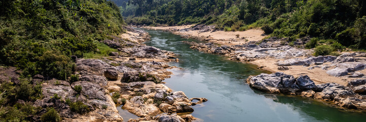 Serpentine river flowing through a rocky landscape with dense tropical forest on the banks,...