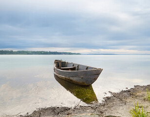 Old wooden fishing boat on the shore of a lake in a cloudy day