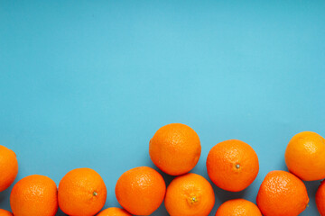 Many fresh orange fruits on light blue background. Vibrant horizontal photo of citrus food with...