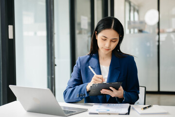 Young beautiful woman typing on tablet and laptop while sitting at the working white table
