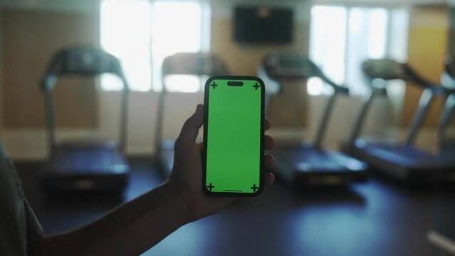 Male hand with smartphone in gym, fitness application results, green screen