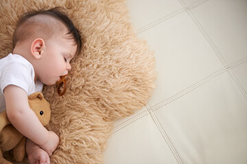 Baby, sleep and cuddle with teddybear on couch at home, rest and relax with dummy and dream. High angle, toddler, and nap in sofa for child development, growth and innocent with peace for bedtime.