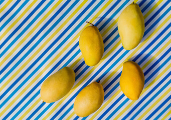 Fresh ripe mangoes on a diagonal striped blue, yellow, and white background, ideal for text overlay and summer-themed designs