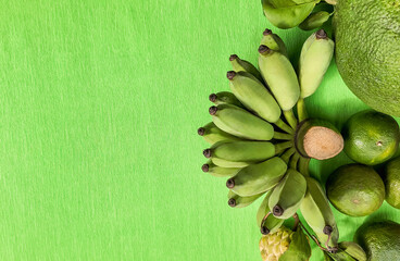 Fresh green bananas, citrus, and avocado on a vibrant green background with space for text, ideal for healthy eating or vegan lifestyle concepts