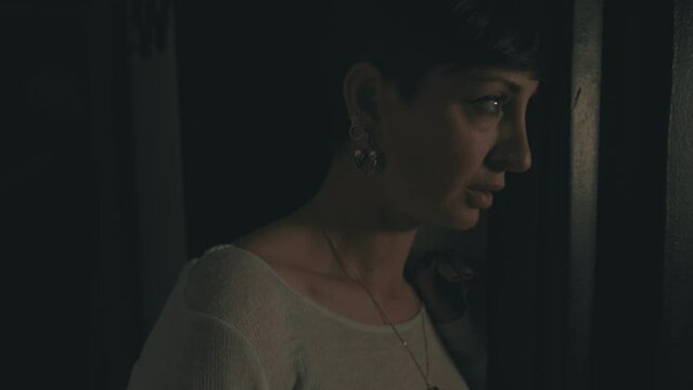 Woman in Darkness: Fearful Gaze into a Dimly Lit Room