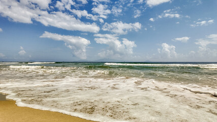 Obraz premium Panoramic view of a serene tropical beach with spacious sandy shore and gentle waves under a blue sky with scattered clouds, ideal for travel backgrounds or holiday concepts, Earth day