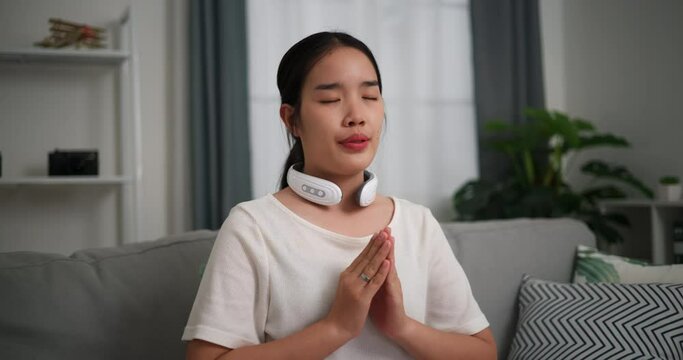 Footage selective focus shot, Relaxed young woman wear automatic massage neck at home with eyes closed, relaxing body and mind alone in the living room, breathing fresh air,