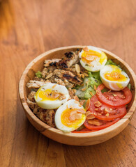 salad with lettuce, tomato and two eggs served on a wooden bowl