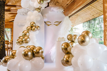 Photo wall decoration of angel wings and white and gold balloons in the hall restaurant. Celebration baptism concept. Trendy cake. Birthday party. Birthday decor for a baby party on white background.