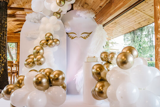 Photo wall decoration of angel wings and white and gold balloons in the hall restaurant. Celebration baptism concept. Trendy cake. Birthday party. Birthday decor for a baby party on white background.