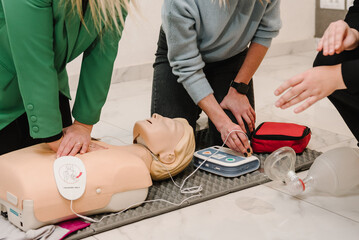 Automated external defibrillator device, AED with training dummy mannequin. Use an automatic defibrillator in conducting basic cardiopulmonary resuscitation of victim. Demonstrating chest compressions - obrazy, fototapety, plakaty