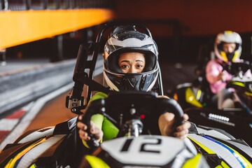 Hispanic latin woman with helmet holding kart steering wheel on karting track driving