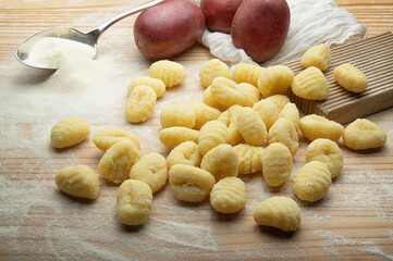Potato gnocchi with durum wheat flour, silver spoon and gnocchi board on pastry board, close-up. - 747905088