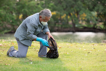 senior man or volunteer wearing face mask holding garbage bag and cleaning in the park