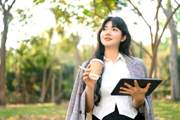 Fototapeta premium Portrait smiling female entrepreneur holding a takeaway paper cup of coffee and looking away at park
