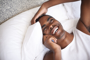 Happy, black man and lying in bed with phone for communication, conversation or networking at home. Face of African male person with smile on mobile smartphone for discussion or relax in the bedroom