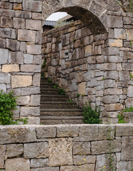 A narrow tunnel-like passage paved with small stones in the walls of a historical fortress.