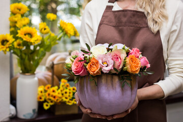 Florist holding a composition of pumpkin and rose flowers in a flower shop close-up