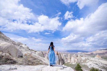 Beautiful woman in blue dress on Turkey rocks mountain.Cheerful woman relax outdoor with beautiful sky and pink flowers in holiday vacation.Woman tourist enjoy amazing mountain view.Travel and freedom