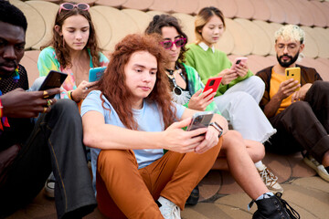 Technology addicted multiracial group young friends using cell phones outdoors with serious face. LGBT diverse community mobile addicts checking social media at gay pride festival. Generation z