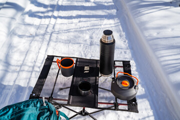 Automotive tire, lighting, and bumper with a thermos and cups on snowy table