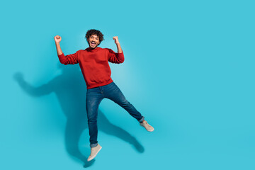 Fototapeta na wymiar Full body size photo of young hispanic man in red sweatshirt and jeans jumping fists up triumphant isolated on aquamarine color background