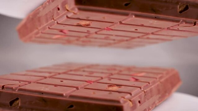 Close-up a milk ruby chocolate bar with chunks of nuts almonds and strawberry, displayed against a gray background is placed on a reflective surface, creating a mirrored image of itself