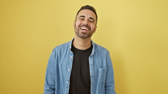 Wacky fun! young hispanic man in denim shirt, sticking tongue out, showcasing a funny expression. unleashing happiness on isolated yellow background.