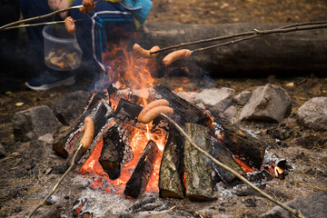 roasting sausages on sticks over a small camp fire