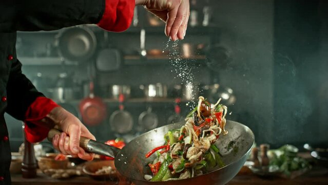 Super Slow Motion of Flying Asian Noodles with Vegetable and Prawns. Chef is Pouring Salt in the Meal. Filmed on High Speed Cinema Camera, 1000 fps.