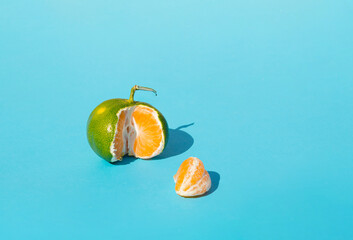 Minimal idea peeled green tangerine on the table. Concept a piece of orange  fruit on blue...