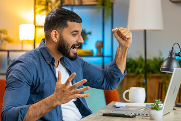 Happy amazed Indian man working on laptop shocked by sudden victory, celebrate game winning, goal...