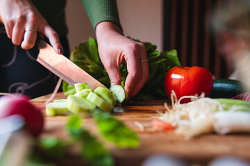A close up of girl's or woman's hands cutting and peeling vegetables with knife making salad