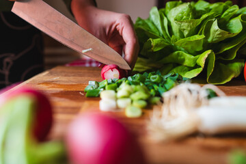 A close up of girl's or woman's hands cutting and peeling vegetables with knife making salad - obrazy, fototapety, plakaty