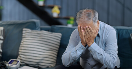 Asian India retired old elder gen x tired upset sad man sitting alone sofa couch feel bad sorrow indoor home Indian aged older adult tense lost male think lonely suffer ill sick health room house