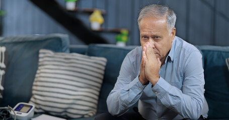 Asian India retired old elder gen x tired upset sad man sitting alone sofa couch feel bad sorrow indoor home Indian aged older adult tense lost male think lonely suffer ill sick health room house
