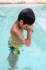 Happy Indian boy swimming in a pool, Kid wearing swimming costume along with air tube during hot summer vacations, Children boy in big swimming pool.