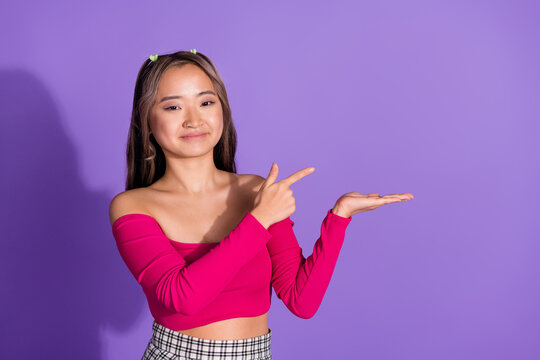 Photo of adorable cheerful girl with ponytails wear stylish crop top indicating at offer on palm empty space isolated on violet background