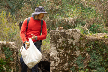 mountaineer with hat picking up garbage in nature.