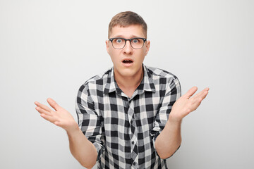 Young man in checkered shirt looking surprised with hands raised on a white background.