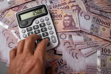 Hungarian HUF banknotes are spread out and sorted on a table, on which a man uses a calculator....