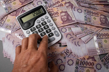 Hungarian HUF banknotes are spread out and sorted on a table, on which a man uses a calculator....
