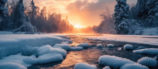Fotobehang A river winds its way through a forest blanketed in snow, creating a stark contrast between the icy waters and the frost-covered trees. The snow-covered landscape glistens in the soft light of the © TheWaterMeloonProjec
